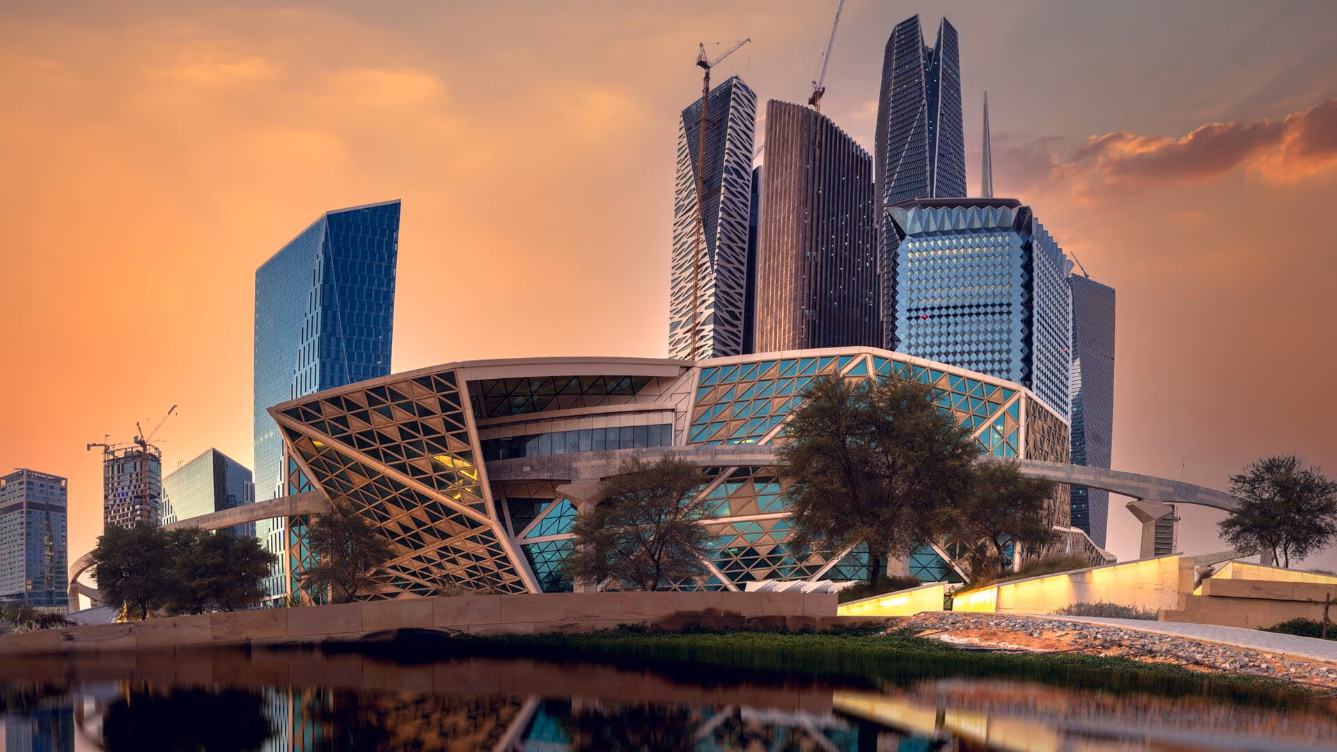 Skyline of Riyadh, Saudi Arabia featuring modern skyscrapers and construction cranes at sunset.